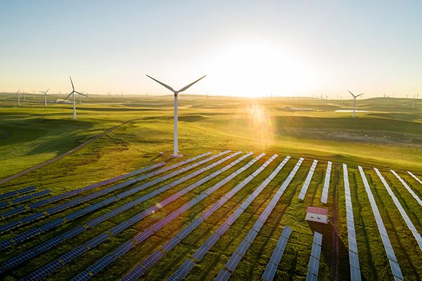 Das Bild stellt ein erneuerbares Energiegebiet dar, bestehend aus Windturbinen und einem großen Feld von Solarpanels.

Beschreibung:
1. **Windturbinen:** Mehrere Windräder sind über die Landschaft verteilt, die den Wind nutzen, um mechanische Energie in elektrische Energie umzuwandeln.
2. **Solarpanels:** Ein weites Feld von Solarpanels sammelt Sonnenenergie und wandelt sie in elektrischen Strom um. Diese Panels sind ordentlich in Reihen aufgestellt.
3. **Umgebung:** Die windgeblasene grüne Landschaft und das sanfte Licht der aufgehenden oder untergehenden Sonne verleihen der Szenerie eine friedliche und harmonische Atmosphäre.
4. **Sonnenlicht:** Der Sonnenstrahl auf der Linse deutet auf eine Nutzung durch Solarenergie hin, und verstärkt den Eindruck von nachhaltiger Energiegewinnung.

**Funktion:**
- Das Bild symbolisiert den Fortschritt in der Nutzung erneuerbarer Energien und die Kombination verschiedener Technologien zur Erschließung umweltfreundlicher Energiequellen.
- Es zeigt die Bemühungen zur Reduzierung des CO2-Fußabdrucks und zur Förderung einer nachhaltigen Zukunft durch die Erzeugung von sauberem Strom.