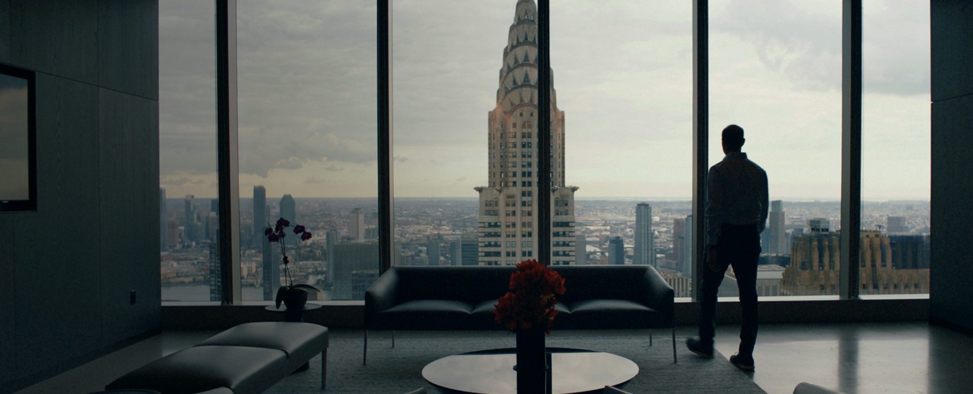 Mann steht vor Fensterfront in einem Wokenkratzer und blickt auf das Chrysler Building in New York.