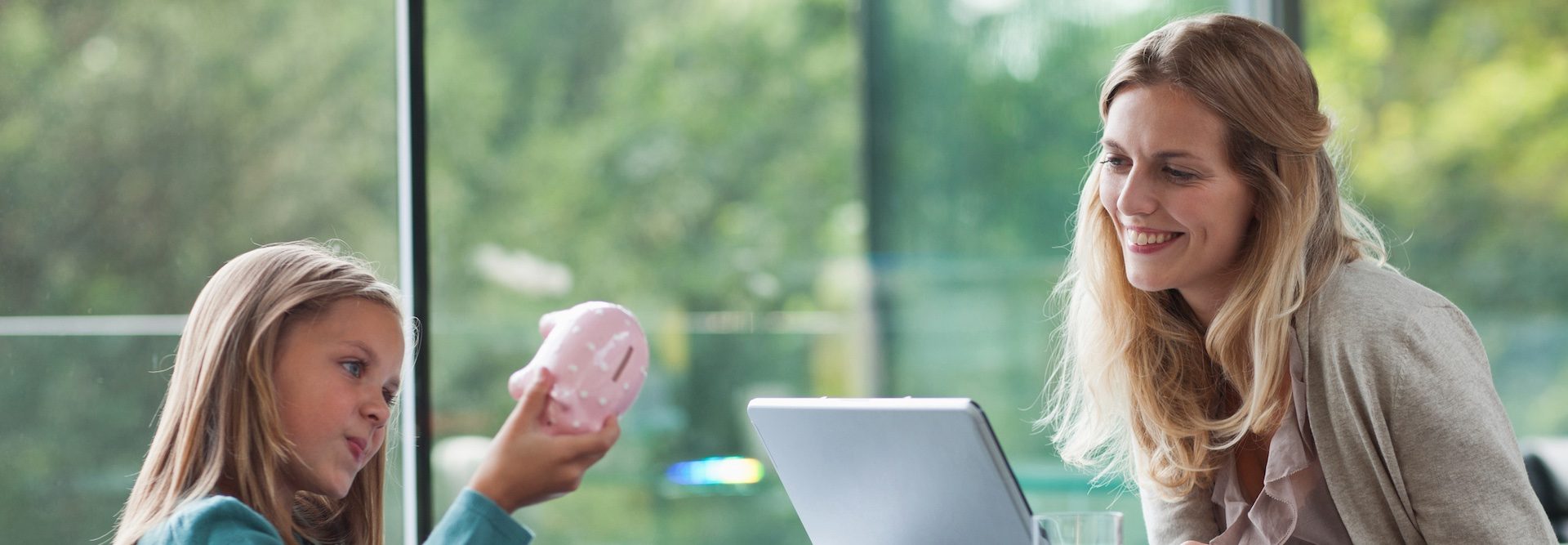 Kind mit Sparschwein und Mutter vor Laptop