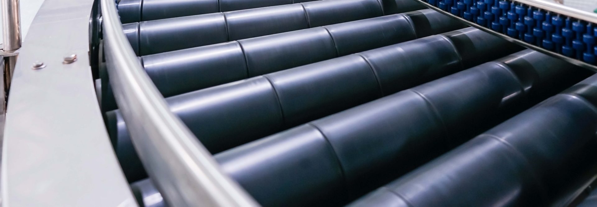 Das Bild zeigt ein Förderband in einer industriellen Umgebung. Das Förderband besteht aus parallel angeordneten Rollen, über die Materialien oder Produkte transportiert werden. Solche Systeme werden häufig in Produktions- oder Logistikanlagen eingesetzt, um die Effizienz bei der Beförderung von Gütern zu steigern. Das System sieht robust und für schwere Lasten geeignet aus. Es scheint ein Teil einer größeren Maschine oder Anlage zu sein.