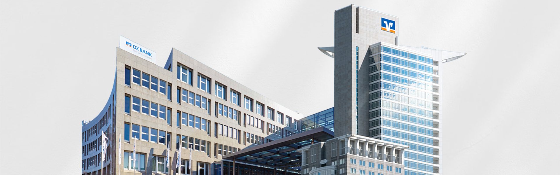 Das Bild zeigt ein modernes Bürogebäude mit mehreren Stockwerken. Auf dem rechten hohen Turm ist das Logo einer Volksbank/Raiffeisenbank sichtbar. Das Gebäude wirkt architektonisch markant und zeitgenössisch.