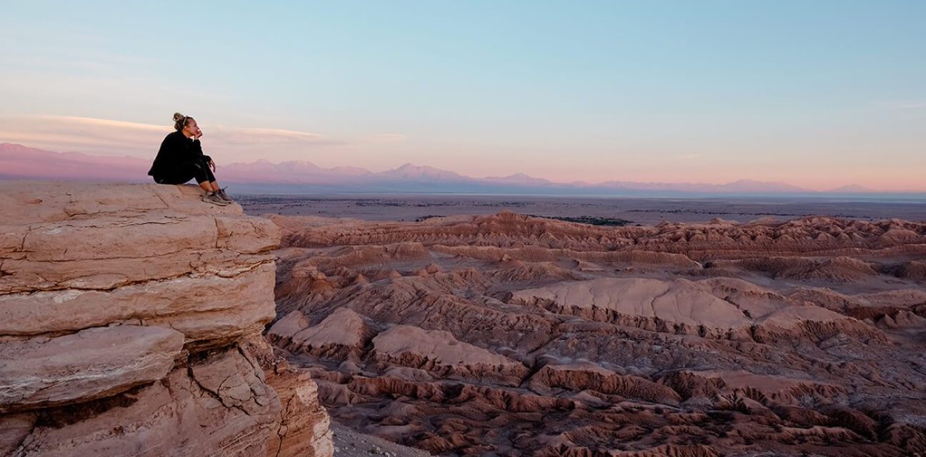 Toma Kubiliute sitzt in der Abenddämmerung auf einem Felsvorsprung und blickt auf die zerfurchte Gebirgslandschaft der Atacama-Wüste in Chile.