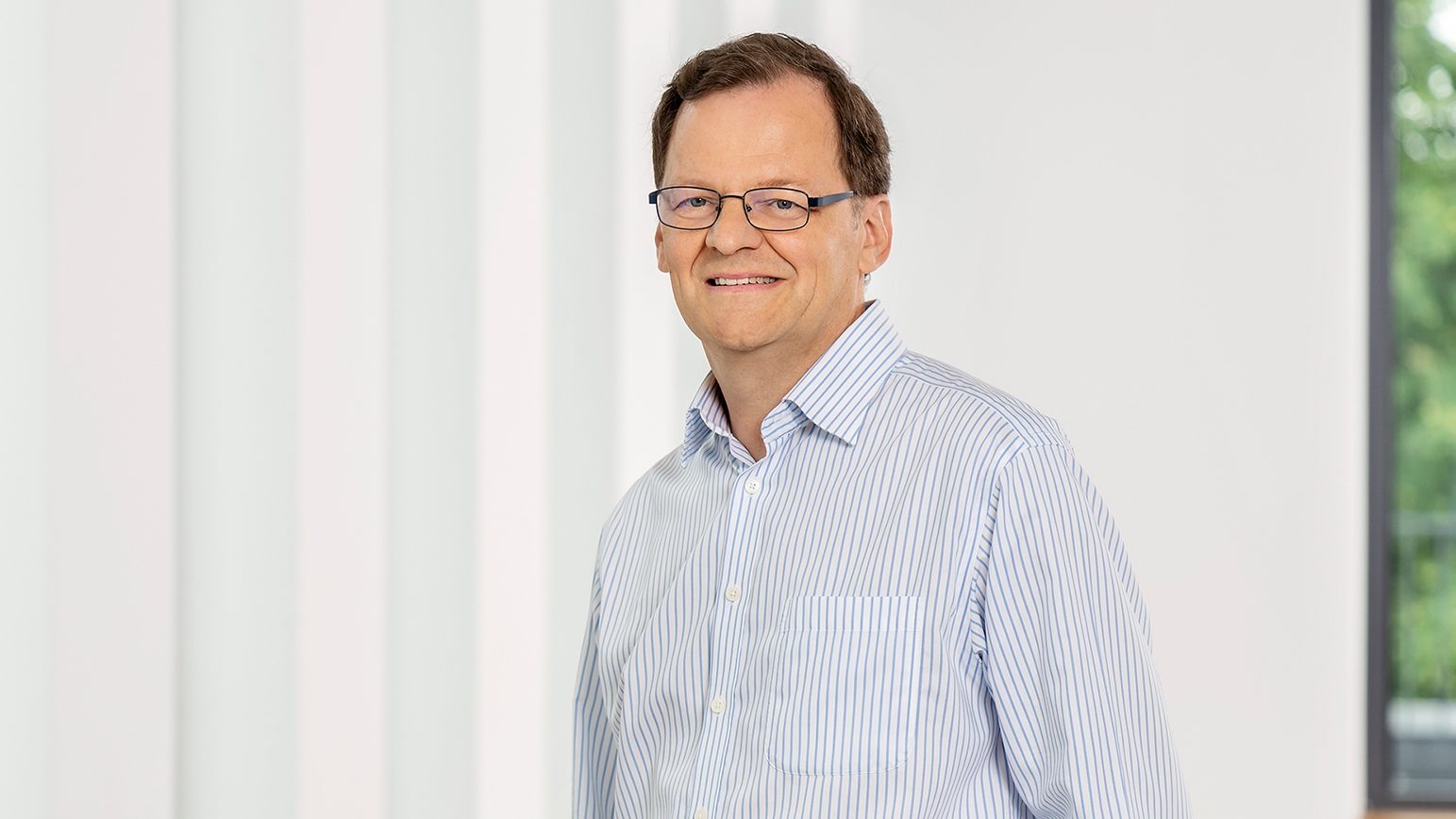 Ein Mann trägt ein hellblau gestreiftes Hemd vor einem hellen Hintergrund.