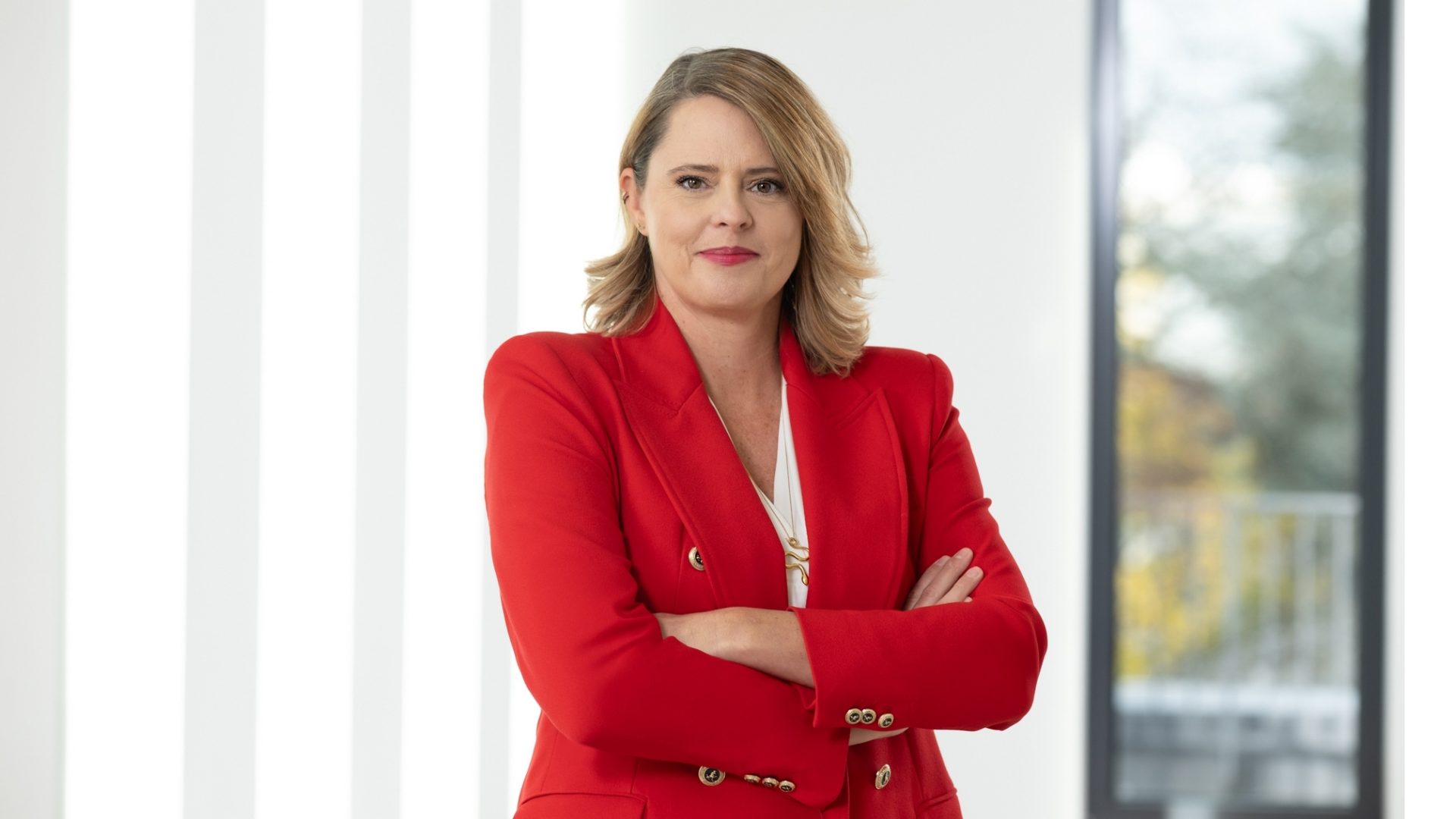 Die Person trägt ein rotes Jackett und steht mit verschränkten Armen.