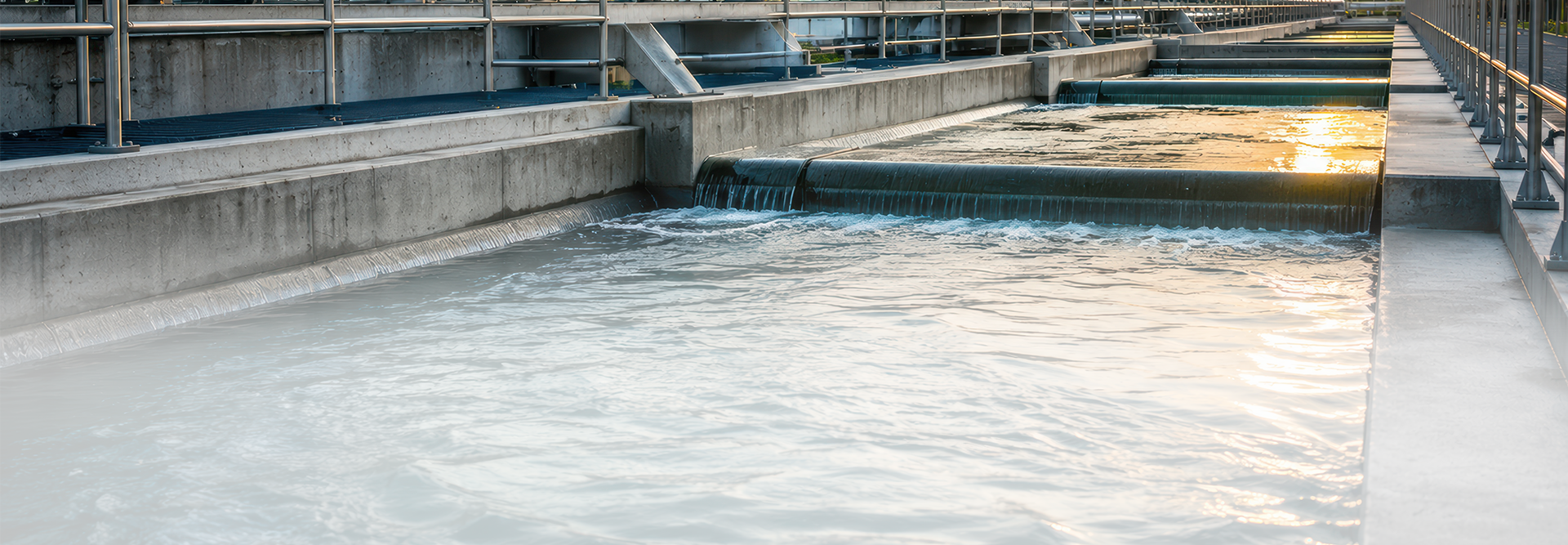Das Bild zeigt vermutlich eine Wasseraufbereitungsanlage oder Kläranlage. Zu sehen sind Becken mit fließendem Wasser, die von Betonwänden umgeben sind, sowie Geländer an den Seiten. Solche Anlagen dienen der Reinigung von Abwasser oder Trinkwasser.