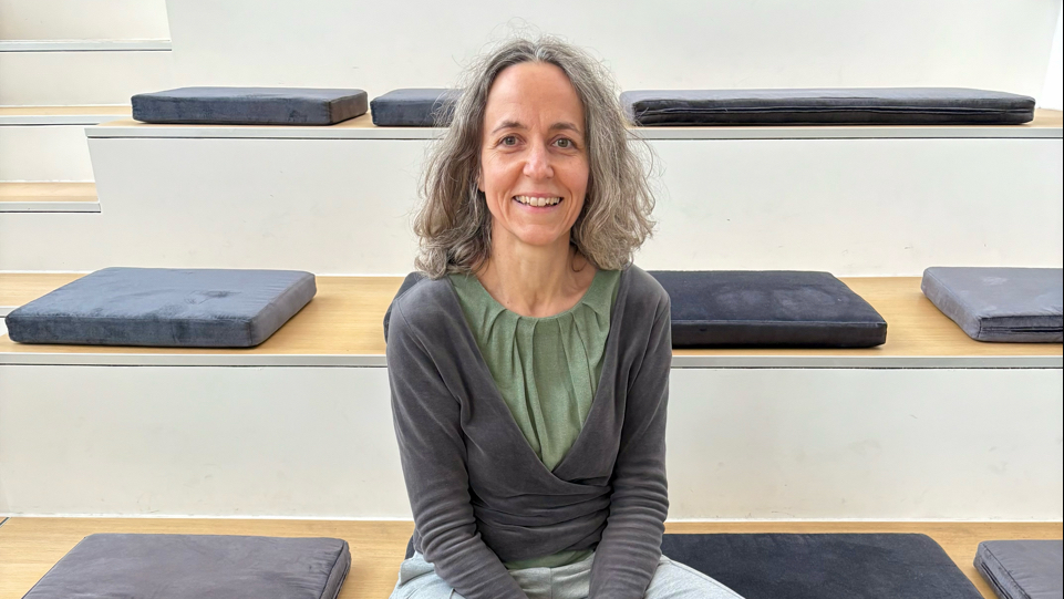 Ein Raum mit hölzernen Stufen, auf denen schwarze und graue Kissen liegen, die möglicherweise für Meditation oder Sitzgelegenheiten gedacht sind.