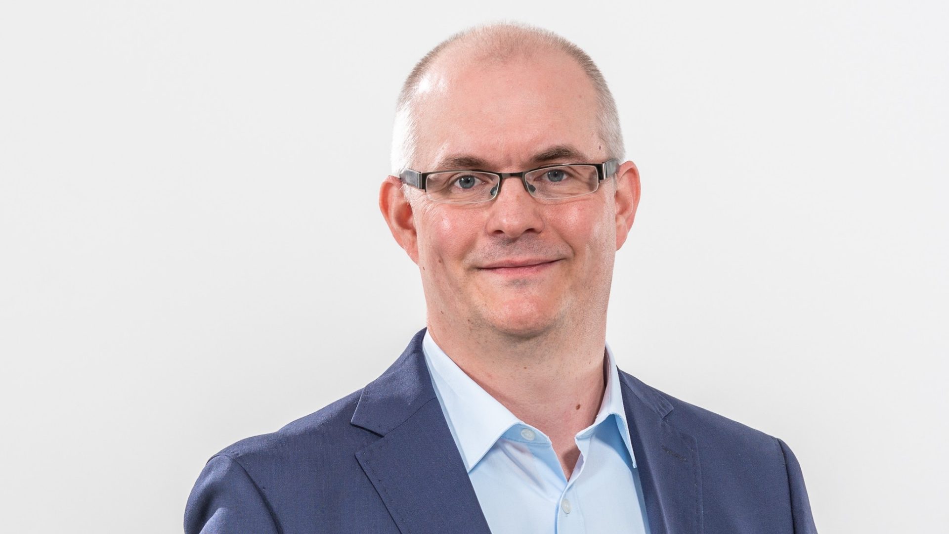 Die abgebildete Person trägt einen hellblauen Hemd und ein dunkles Sakko. Der Hintergrund ist einfarbig weiß.