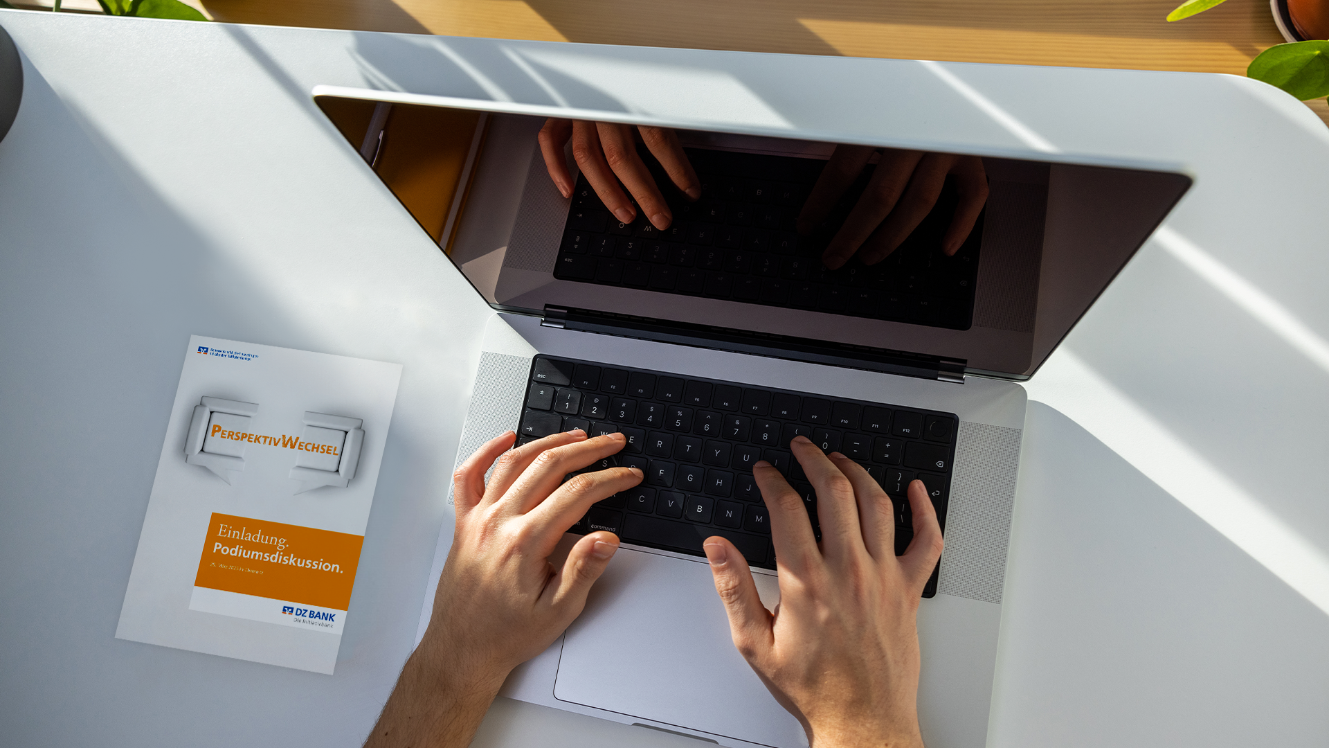 Das Bild zeigt eine Person, die an einem Laptop arbeitet. Die Hände der Person befinden sich auf der Tastatur, und das Display des Laptops reflektiert die Hände. Neben dem Laptop liegt eine Broschüre oder ein Infoblatt mit dem Titel "Kosten-Nutzen Analysen", was darauf hinweisen könnte, dass die Person an einer Analyse, Recherche oder im Rahmen eines wirtschaftlichen Projekts arbeitet. Der Raum um den Laptop ist gut beleuchtet, möglicherweise durch Tageslicht, das für eine angenehme Arbeitsumgebung sorgt. Auch sind Pflanzen am Rand des Bildes zu sehen, die eine natürliche und beruhigende Atmosphäre schaffen.